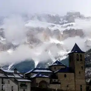 Pueblo pirenaico de piedra bajo montañas nevadas y niebla en Ordesa